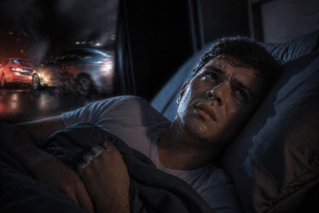 A person lies awake in a dark bedroom, looking anxious and distressed, with visible sweat on their face. Blurred car accident lights and motion appear in the background, symbolizing traumatic flashbacks, while cinematic lighting highlights the emotional intensity of the scene.